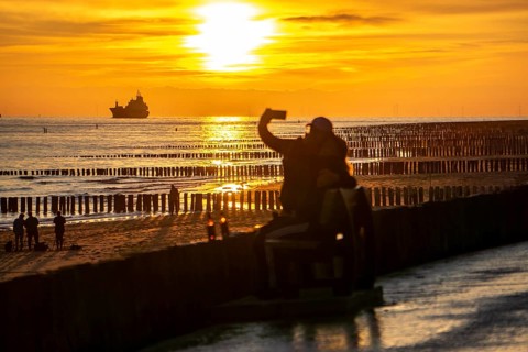 Sunset on the beach of Zoutelande, beach with wooden pile breakwaters, tourists, cargo ship sailing