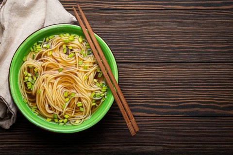 Asian noodles soup in green rustic ceramic bowl with wooden chopsticks top view on dark wooden