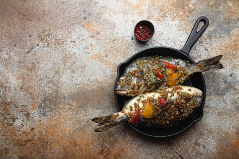 Two raw fishes dorado stuffed with vegetables and seasonings ready to be cooked laying in black
