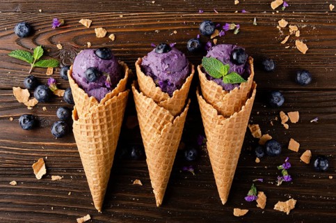 Flat lay view at wafer cones with blackberry icecream on wooden kitchen table
