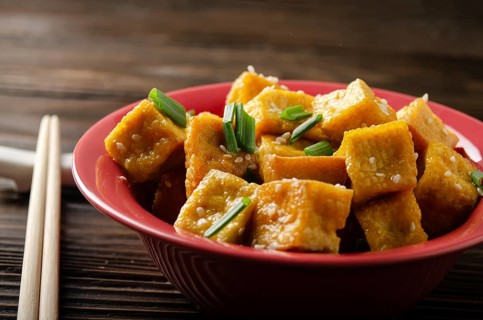 Crispy deep stir fried tofu cubes with chives in clay dish on wooden kitchen table