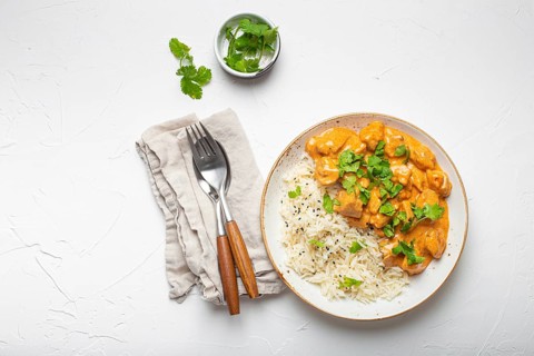 Traditional Indian dish chicken curry with basmati rice and fresh cilantro on rustic white plate on