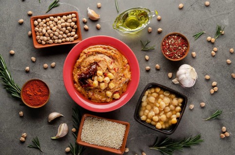 Hummus topped with chickpeas, olive oil and sun dried tomato on stone table with different spices