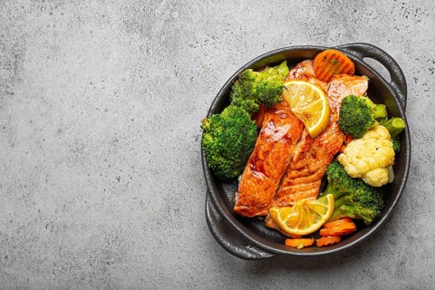 Healthy baked fish salmon steaks, broccoli, cauliflower, carrot in black cast iron casserole bowl