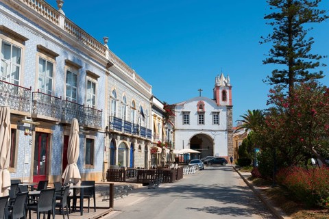 Cosy street lined with buildings and cafés, in the background a church under a clear sky, on the