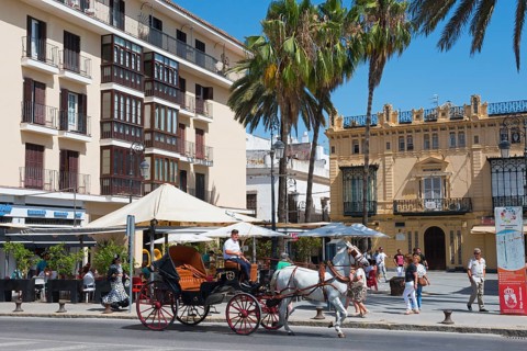 Horse-drawn carriage with passengers on a sunny street, surrounded by old buildings, Sanlúcar de