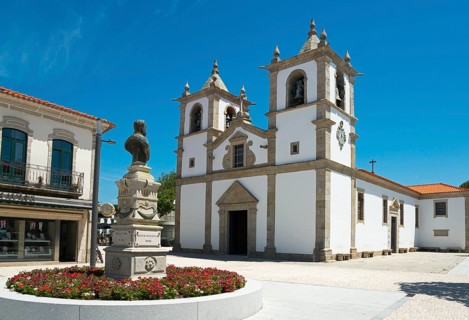 A church with a double tower stands on a sunny square with a flower bed, Igreja Matriz de