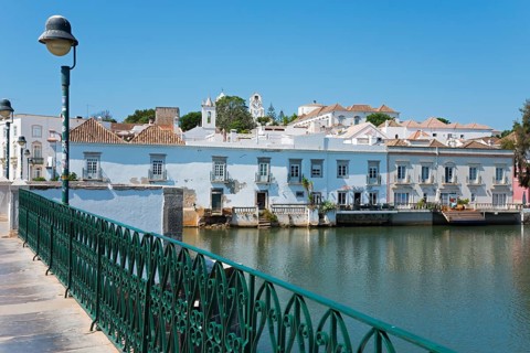 Bridge with green railing along a calm river, historical buildings in the background, Ponte Romana,