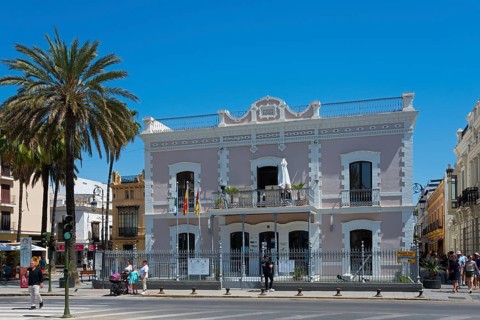 Large historical building with palm trees in front of it, people at a crossroads, Ayuntamentio,