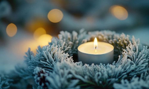A candle is lit in a wreath of pine needles. The candle is surrounded by snow and pine needles,