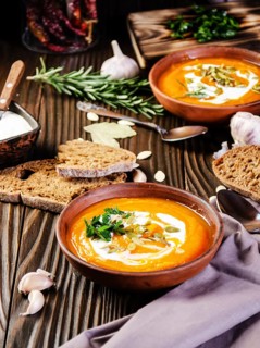 Homemade rustic pumpkin soup with seeds in clay dish on wooden table with bread spices and greens