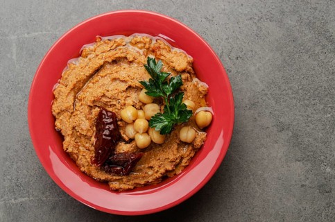 Flat lay view at hummus topped with chickpeas, sun dried tomatoes and green coriander leaves on