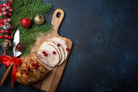 Christmas baked ham sliced with red berries and festive decorations on wooden cutting board, dark