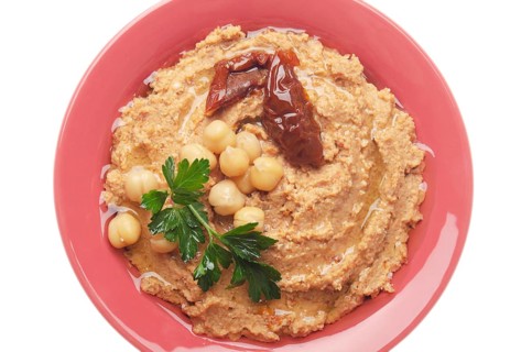 Flat lay view at hummus topped with beans, sun dried tomatoes and green coriander leaves isolated