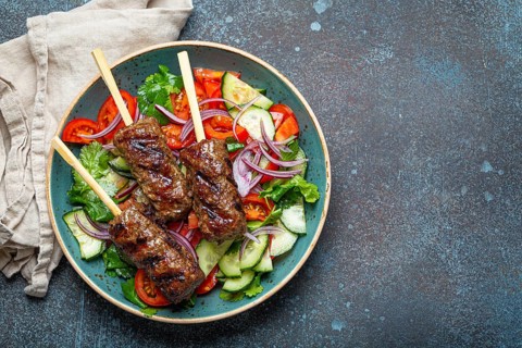 Grilled skewer meat beef kebabs on sticks served with fresh vegetables salad on plate on rustic