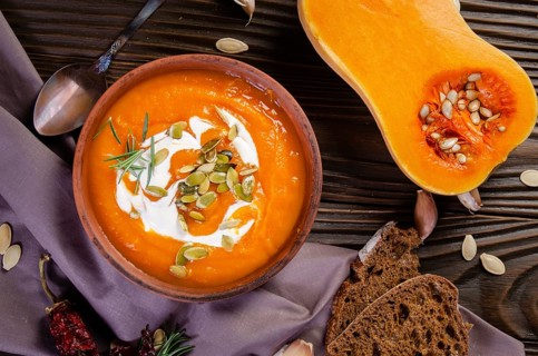 Flat lay view at homemade rustic pumpkin soup with seeds in clay dish on wooden table with bread