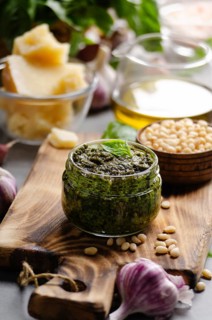 Glass jar with genovese pesto sauce on cutting board with basil leaves, pine nuts, parmesan cheese,