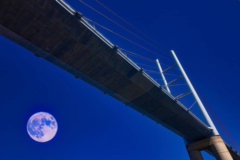 A modern bridge at night, illuminated by a clear sky with a full moon, Rügenbrücke, Stralsund,