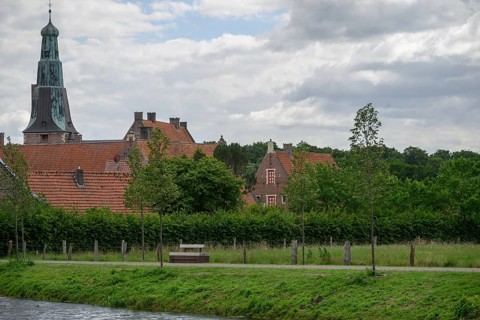 Quiet village scene with church tower, red roofs, green trees and a watercourse under a partly