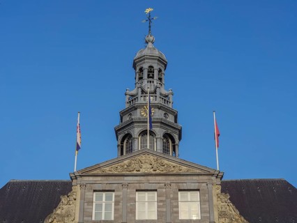 Close-up of a tower with complex architecture and two flags against a blue sky, maastricht.