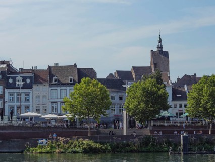 Riverbank with historic buildings, trees and people enjoying the surroundings, maastricht.