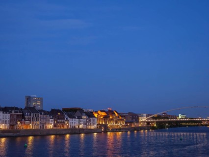 Riverbank with illuminated houses and a bridge during the blue hour, maastricht, the netherlands