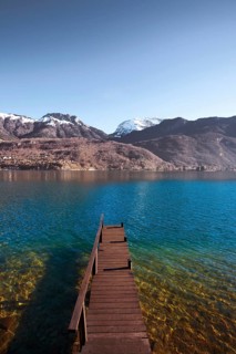 An old wooden pier faces the snow-capped mountains of the French alps on beautiful Lake Annecy.