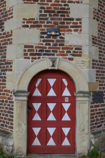 Historic red wooden door with white triangular patterns in a stone wall with bricks, Raesfeld,