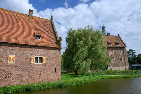 Historic castle with red tiled roofs and a moat, surrounded by trees and clouds, Raesfeld, North
