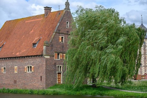 Small half-timbered building with red tiled roof by a moat, surrounded by green trees, Raesfeld,