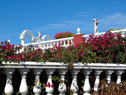 White balustrade with pink flowers and architecture in the background on a sunny day, puerto de la