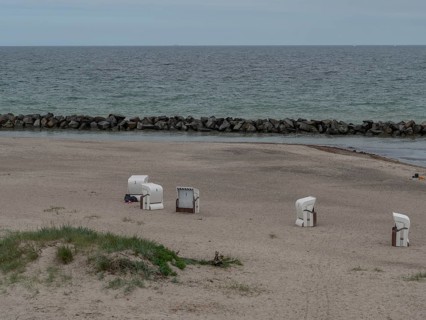 An empty beach with a few beach chairs, a calm sea and stone breakwaters in the background. A quiet