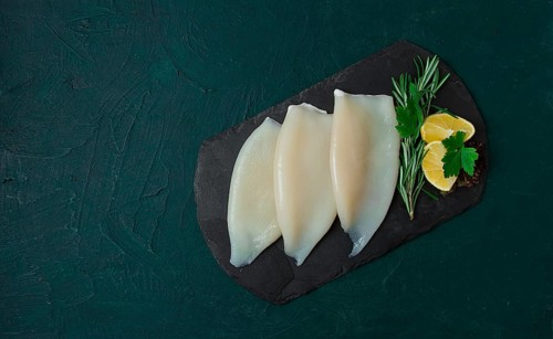 Fresh squid body, raw, three carcasses, top view, on black slate, no people