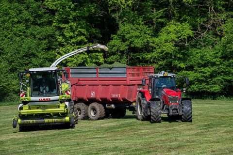 Tractor with trailer running beside Claas Jaguar 870 forage harvester, self-propelled silage