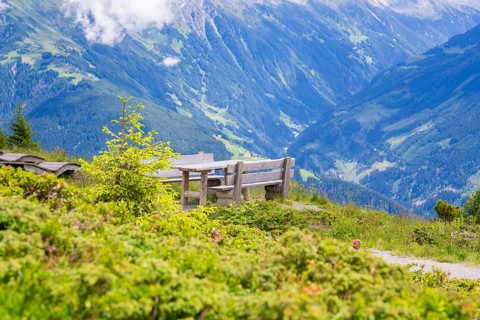 A bench on a hill with a view of the impressive mountain landscape under a partly cloudy sky,