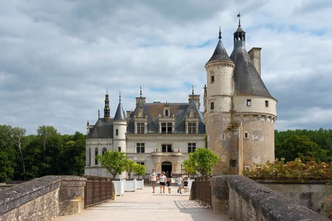 Imposing castle with tower and visitors on the bridge in front of a cloudy sky, Chenonceau Castle,