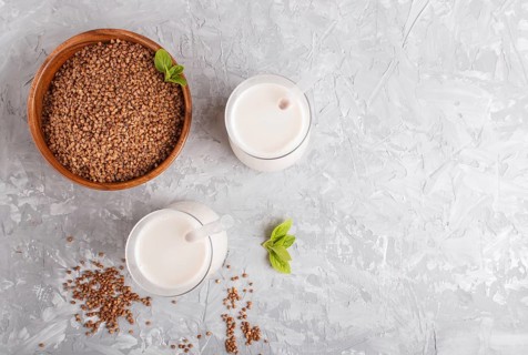 Organic non dairy buckwheat milk in glass and wooden plate with buckwheat seeds on a gray concrete