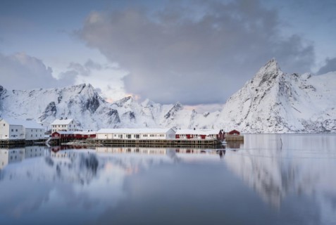 Rorbuer huts of Hamnoy at the fjord, snowy mountains in the background, Hamnøy, Reine, Moskenesøya,