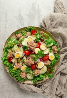 Tuna salad, vegetable salad with quail eggs, lettuce, red onion and cucumbers, on a light gray