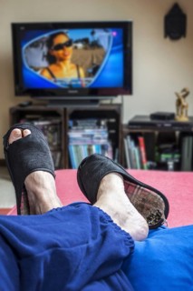 Couch potato, lazy man in comfy chair wearing worn slippers with big toes sticking through and