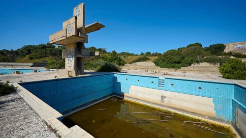 Old abandoned swimming pool with graffiti and algae-infested water, surrounded by nature on a sunny