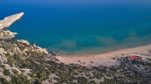 Aerial view of a secluded beach with clear water and small huts on the shore, Tsambika Beach,
