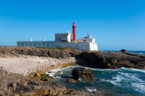 Old lighthouse on a rocky coast under a clear blue sky, Farol do Cabo Raso, São Brás de Sanxete