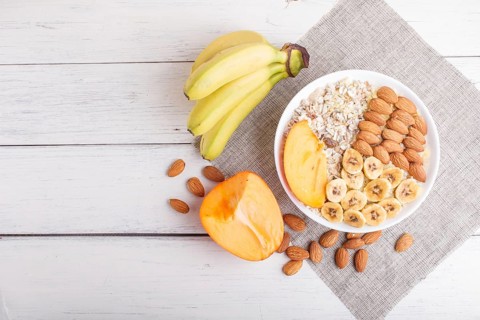 A plate with muesli, almonds, banana, sliced persimmon on a white wooden background. top view. copy