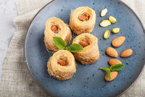 Kunafa, traditional arabic sweets in blue ceramic plate on a gray concrete background. side view,