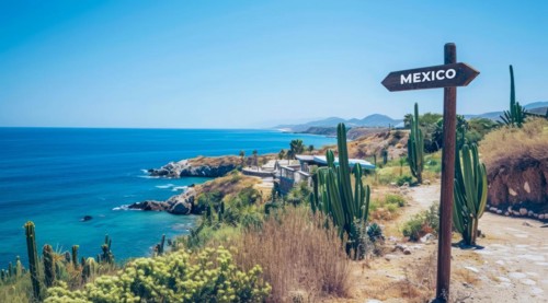 Sign pointing to the direction of Mexico with scenic beach and ocean in the background, AI