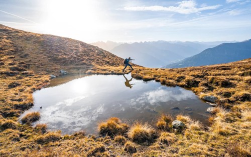 Mountaineer jumping, reflected in a small mountain lake on the Krahberg, mountain panorama in