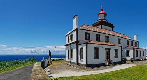 A white lighthouse with red roofs and a display by the sea under a clear blue sky, Farol da