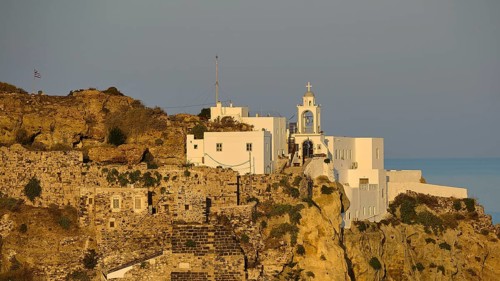 A castle and white buildings on a cliff, illuminated by the golden light of dawn with the sea in