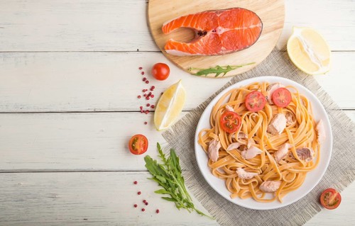 Semolina pasta with salmon and salmon steak on a white wooden background and linen textile. Top
